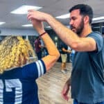 Dancing instructor teaching salsa dance steps to a student in a lively dance class at Salsa Dallas studio.