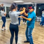 Salsa Dallas dance class with students and instructor practicing salsa moves in a spacious studio. Participants are dancing in pairs, enjoying lively salsa lessons in a professional setting.