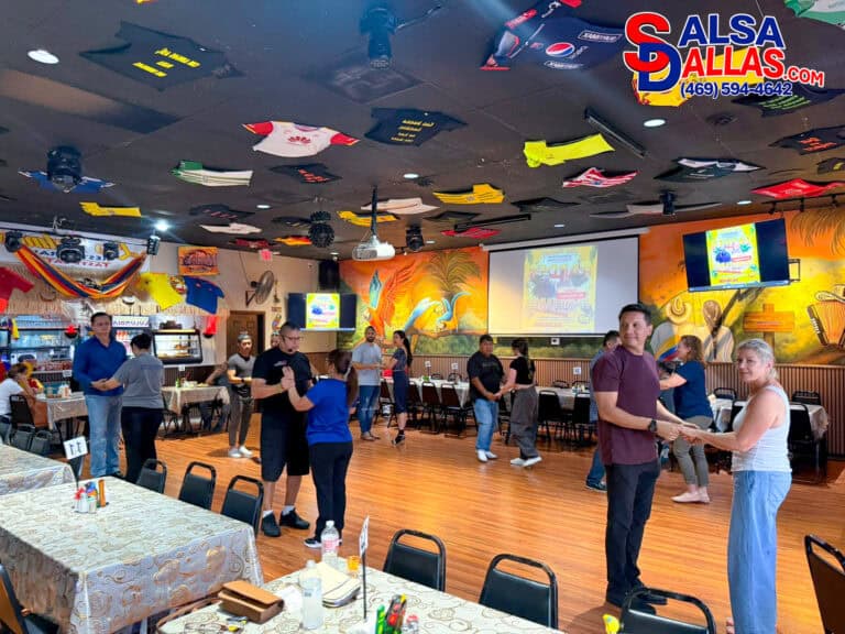 Salsa Dallas dance class with couples dancing in a lively restaurant setting, colorful tropical mural, and vibrant decor, promoting salsa lessons and dance events in Dallas.